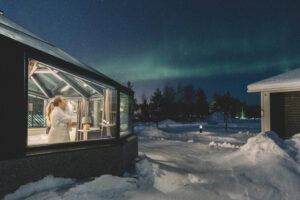 Glass igloo outside in winter, a woman looking at the northern lights inside
