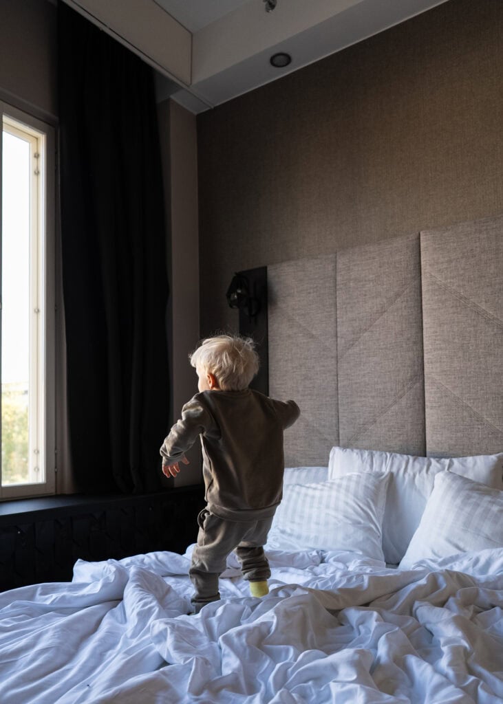 Pieni lapsi hyppii hotellihuoneen sängyllä